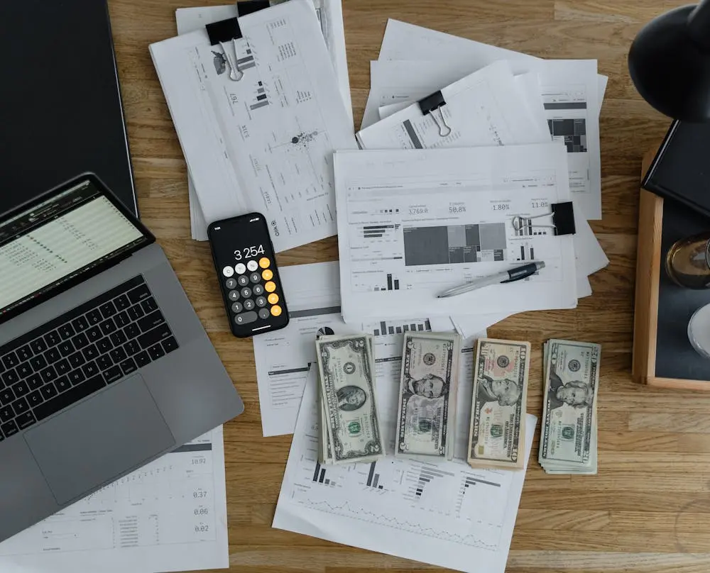 A laptop near the dollars and papers on a wooden table